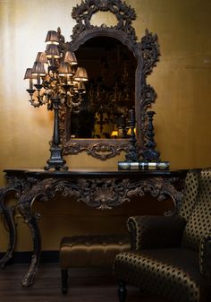 a chair and table with a mirror on it in front of a wall mounted lamp