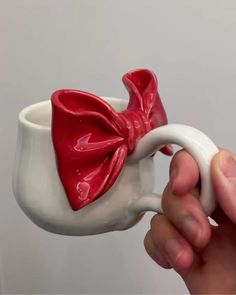 a hand holding a ceramic cup with a red bow on it