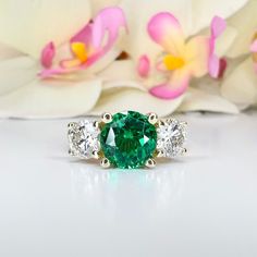 an emerald and diamond three stone ring with flowers in the background