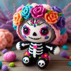 a small crocheted skeleton doll with flowers on it's head sitting next to balls of yarn