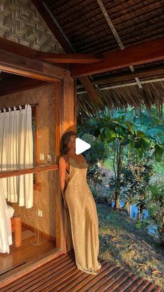 a woman is standing in the open door of a hut looking out at trees and water