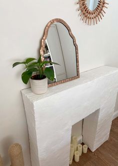 a white fireplace mantle with a mirror and potted plant next to it on top