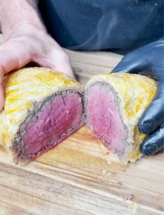 a person is holding a piece of meat on a wooden cutting board with black gloves