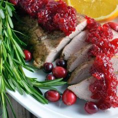 meat with cranberry sauce on a white plate next to lemons and rosemary