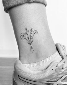 a small flower tattoo on the side of a woman's ankle, with text below it