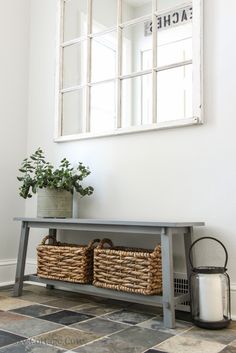 a gray bench sitting next to a window with baskets on it's sides and a mirror above it