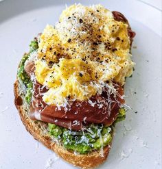 an open face sandwich with eggs, meat and cheese on it sitting on a white plate