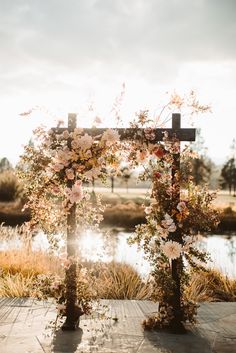 an outdoor ceremony setup with flowers on the cross and water in the background at sunset