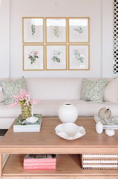 a living room with white couches and pictures on the wall above them, along with pink flowers in vases