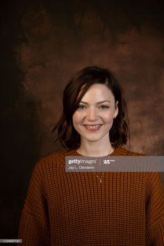 a woman smiling and wearing an orange sweater