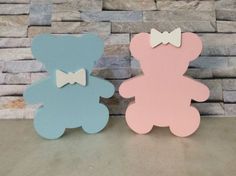 two wooden teddy bears with bow ties on their ears, one is pink and the other is blue