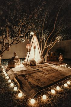 a teepee is lit up in the dark with candles around it and lights on the ground