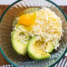 an avocado and cheese dish in a glass bowl on top of a wooden table