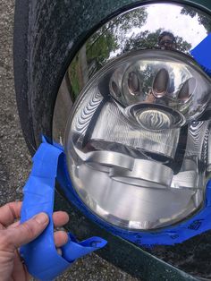 a close up of a person's hand holding scissors near a car headlight