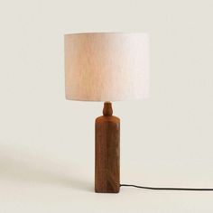 a wooden table lamp with a white shade on the base and a black cord attached to it