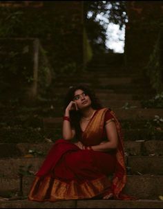 a woman in a red and gold sari sitting on steps talking on her cell phone