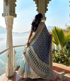 a woman in a blue and white lehenga looking out over the water from a gazebo