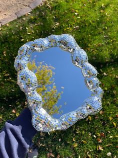 a mirror sitting on top of a lush green field next to a leaf covered park