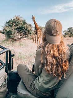 a woman sitting in the back of a truck watching a giraffe