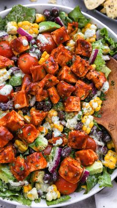 a salad with chicken, tomatoes, lettuce, corn and feta cheese