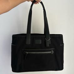 a person is holding a black handbag with zippers on the front and side