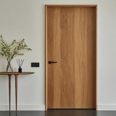 a wooden door in a white room next to a small table with flowers on it