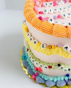 a multi layer cake with letters and numbers on the top, decorated in pastel colors