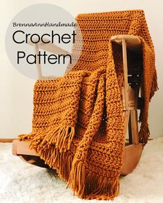 an orange crochet blanket sitting on top of a wooden chair next to a white wall