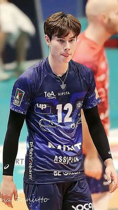 a male volleyball player is wearing blue and has his hands in his pockets as he walks on the court