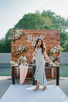 a woman standing in front of a wooden sign with flowers and wine glasses on it