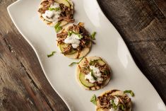 four tacos with meat, cucumber and sour cream on them sitting on a white plate