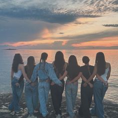 four women standing on the edge of a cliff looking out to sea at sunset or sunrise