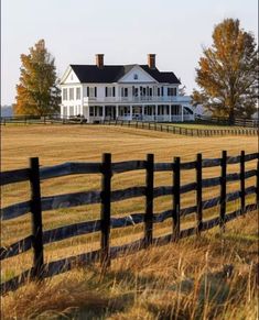 a large white house sitting on top of a lush green field next to a wooden fence