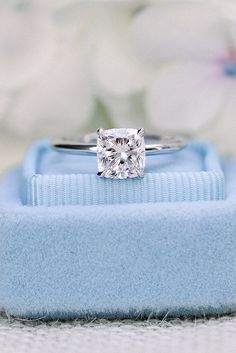 a diamond engagement ring sitting on top of a blue velvet box with flowers in the background