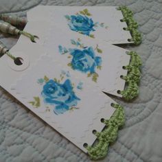 three tags with blue roses on them are sitting on a quilted surface next to scissors