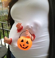 a pregnant woman wearing a white shirt and holding a pumpkin shaped bag with blood on it