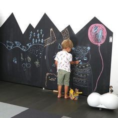 a little boy standing in front of a chalkboard wall with animals and balloons on it