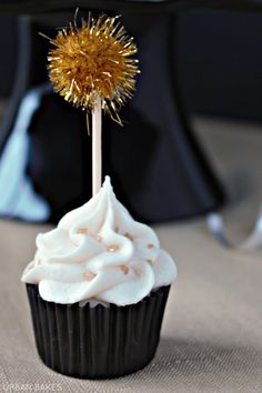 a cupcake topped with white frosting and a gold sprinkle on top