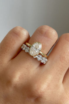 a woman's hand with a diamond ring on top of her finger and the other hand holding an engagement ring