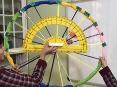 two people are working on a large yellow and green wheel that is being held by a ruler