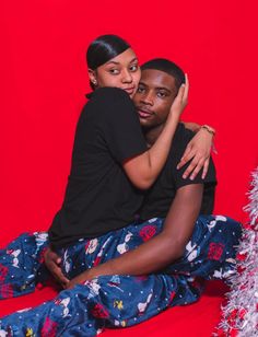 a man and woman sitting on the floor hugging each other in front of a christmas tree