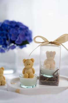 two small teddy bears sitting in glass vases on a white tablecloth with blue flowers