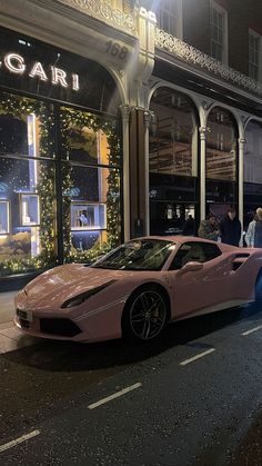 a pink sports car parked in front of a luxury store at night with people walking by