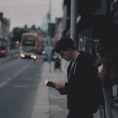 a man is standing on the sidewalk looking at his cell phone while holding something in his hand