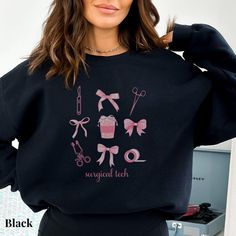 a woman wearing a black sweatshirt with pink bows and scissors on it, standing in front of a mirror