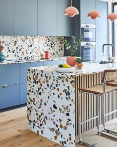 an island in the middle of a kitchen with lots of counter space and hanging lights