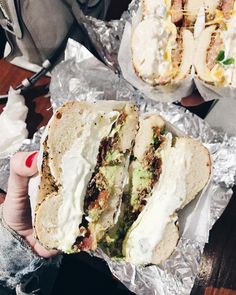 a person holding a half eaten sandwich in their hand on tin foil with other food items behind them