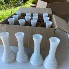 several white vases are sitting in a box on a table outside with grass and trees in the background