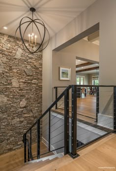 an open staircase leading to a living room with stone wall and wood flooring, along with a chandelier hanging from the ceiling