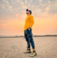 a man standing on top of a sandy beach next to the ocean wearing yellow shoes